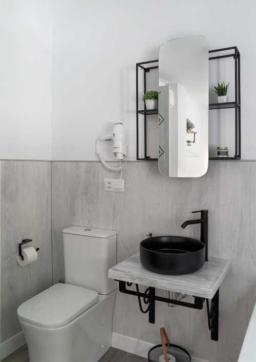 Baño moderno con lavabo negro, inodoro blanco y estanterías del hotel Casa Rural Las Cuevas De Setenil en Cádiz