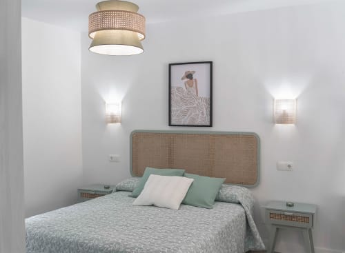 Dormitorio moderno en Casa Rural Las Cuevas de Setenil con cabecero de rattán, ropa de cama salvia e iluminación contemporánea
