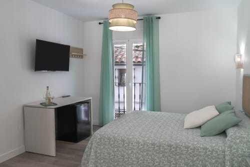 Dormitorio moderno en Casa Rural Las Cuevas De Setenil con TV, minibar, puertas al balcón con cortinas verdes, lámpara colgante y