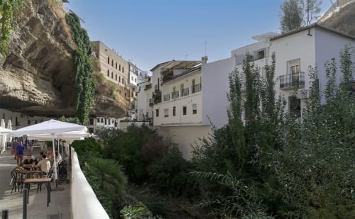 Terraza de Casa Rural Las Cuevas De Setenil con sombrillas blancas frente a edificios blancos integrados en viviendas acantiladas