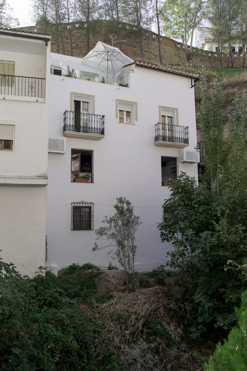 Edificio rural de hotel de paredes blancas en Setenil de las Bodegas con balcones de hierro forjado y telón de fondo de fortaleza de piedra