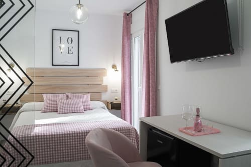 Moderno dormitorio en Casa Rural Las Cuevas De Setenil con ropa de cama a cuadros rosa, cabecero de madera, TV y decoración elegante