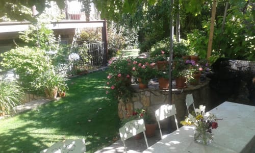 Vue du jardin de Casa Rural La Perla avec terrasse, pelouse verdoyante, fleurs en pots et architecture de maison de campagne