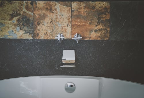 Bagno moderno con vasca bianca e piastrelle in marmo scuro presso Casa Ziazì, hotel a Monopoli, con arte rustica murale e finiture cromate