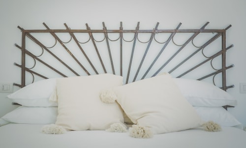 Lussuoso letto con cuscini bianchi e coperte color crema davanti una testiera in metallo a motivo raggi di sole a Casa Ziazì a Monopoli