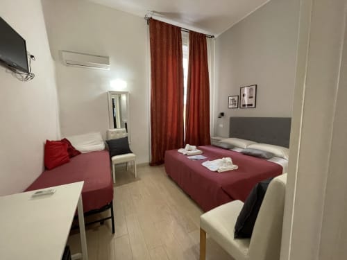 Modern guest room at AD Trastevere Guest House in Rome with burgundy bed, sofa, TV, and red curtains