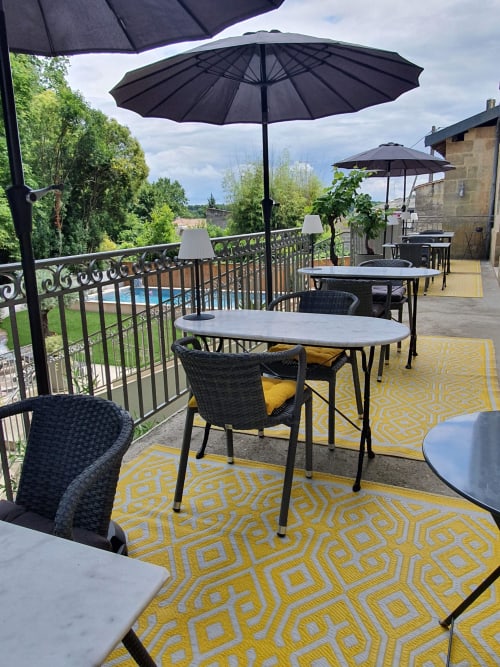 Outdoor terrace at Pavillon Des Millesimes with umbrella-shaded tables, yellow patterned rugs, and vineyard views in Lussac,