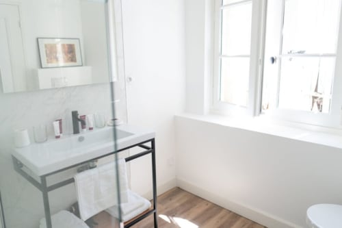 Bright modern bathroom at Pavillon Des Millesimes with white marble vanity, glass shower enclosure, and natural light from