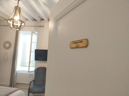 Impériale room at Pavillon Des Millesimes with brass pendant light, white exposed beams, and room number plaque
