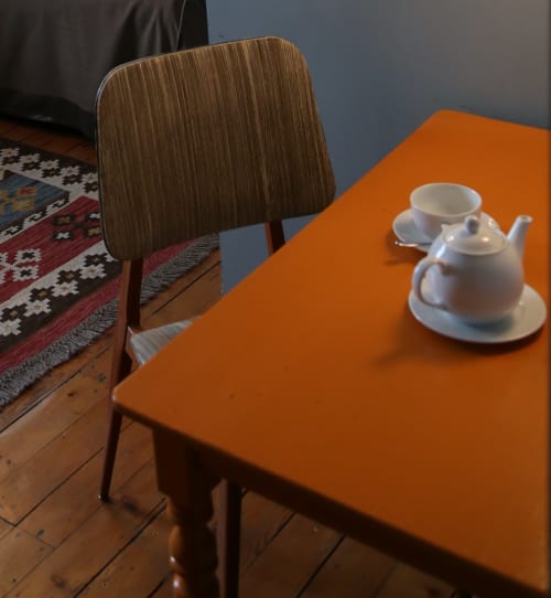 Orange table with white teapot and cup at Le Grand Duc, a B&B in Valenciennes, with wooden chair and city view
