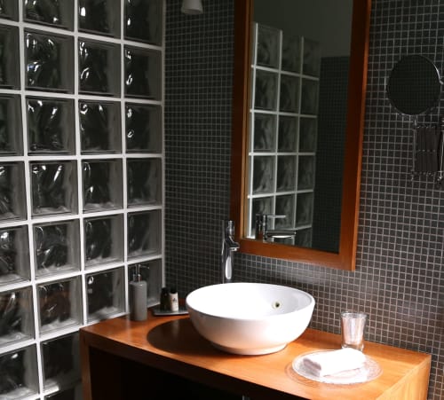 Modern bathroom with white vessel sink on wooden counter, dark tile walls, and glass block shower at Le Grand Duc,