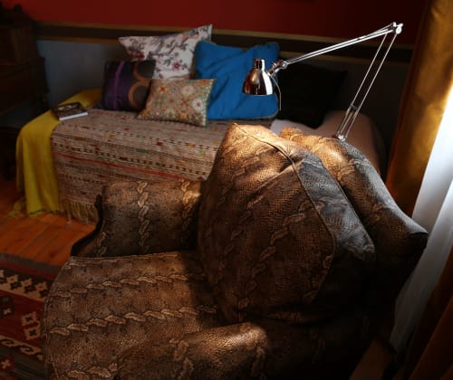Cozy bedroom at Le Grand Duc B&B in Valenciennes with brown armchair, desk lamp, and bed with colorful pillows