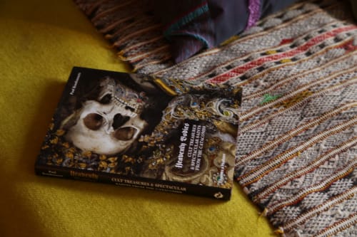 Decorative book with ornate mask on yellow surface beside patterned textile at Le Grand Duc boutique hotel in Valenciennes