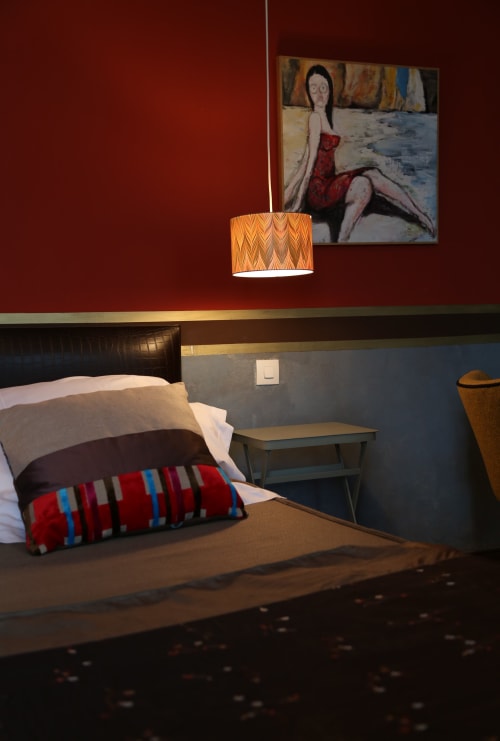 Modern hotel bedroom at Le Grand Duc with bed, striped pillow, pendant lamp, and contemporary artwork on burgundy wall