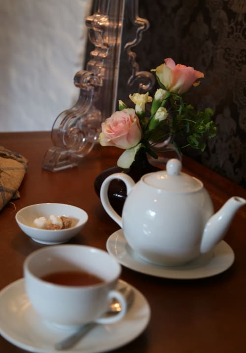 Service à thé élégant au Grand Duc avec pâtisseries, théière blanche et roses fraîches sur table en bois