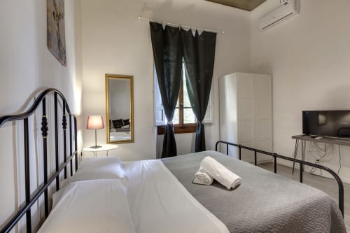 Modern Florence apartment bedroom with twin beds, balcony view, flat-screen TV, and garden-facing windows with dark curtains