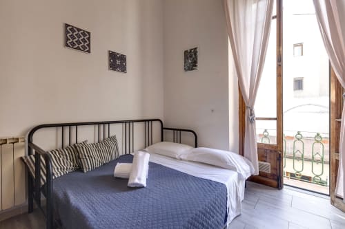 Bright bedroom with black metal bed frame, blue bedding, striped pillows, and balcony overlooking Florence garden in Sleep