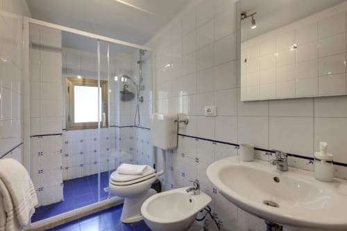 Modern bathroom in Florence apartment with dual sinks, toilet, bidet, glass shower enclosure, and blue tile accents