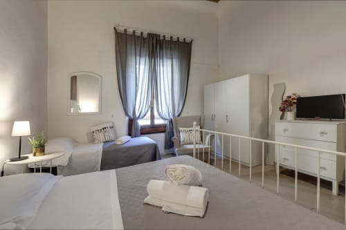 Sleep tight Florence ground floor apartment in Firenze with twin beds, white furniture, TV, and blue curtains at window