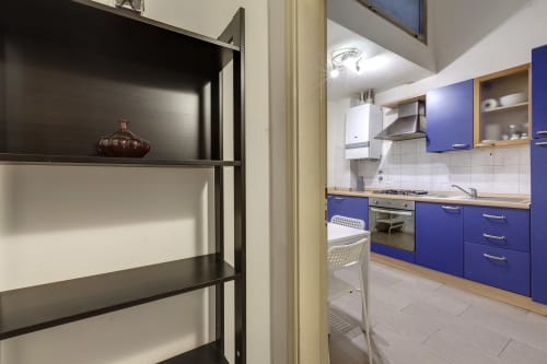 Modern blue kitchen with wooden countertops, white appliances, and open shelving in Florence apartment