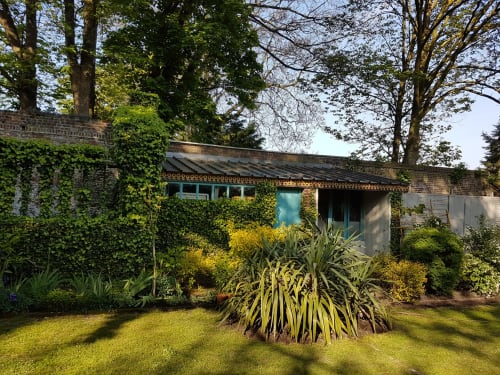 Le jardin du Grand Duc B&B à Valenciennes : bâtiment de briques recouvert de lierre, portes turquoise et paysage verdoyant
