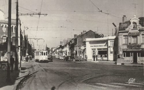 Vue historique d'une rue de Valenciennes avec rails de tramway et devantures anciennes, dont une station-service Esso