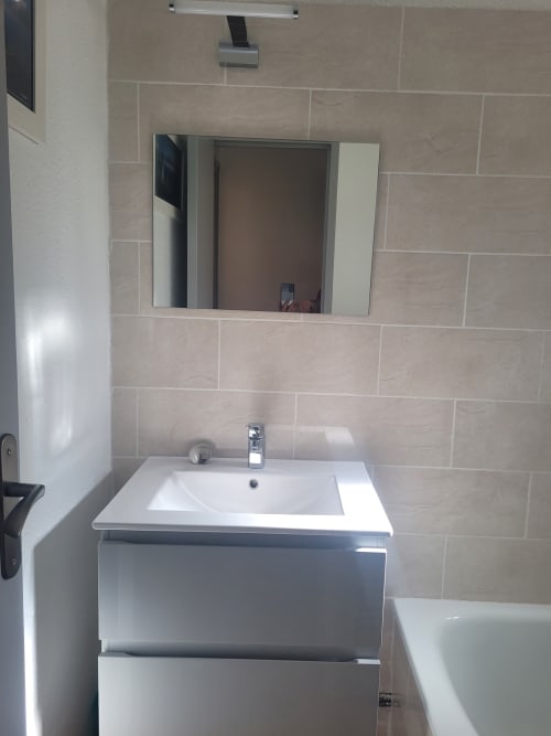 Salle de bain moderne de l'appartement de Porticcio avec lavabo blanc, miroir et murs en carrelage beige