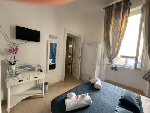 Camera luminosa all'AD Trastevere Guest House di Roma con biancheria blu, mobili bianchi e ampia finestra con tende