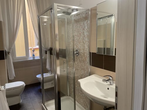 Bagno moderno in una guest house a Trastevere Roma con doccia in vetro, lavabo bianco e pavimento in piastrelle scure