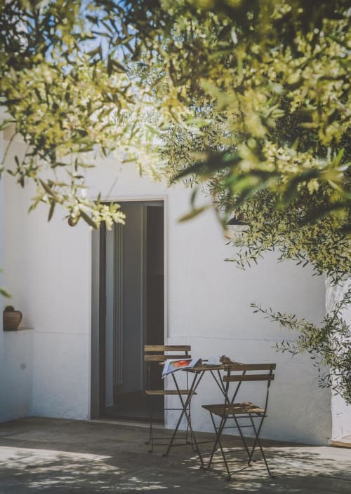 Patio soleggiato di Casa Ziazì a Monopoli con sedie pieghevoli, tavolo in legno e rami di ulivo in alto