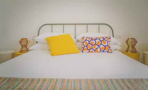 Camera moderna di Casa Ziazì con letto in ferro, cuscini gialli e fantasia, biancheria bianca e comodini in legno
