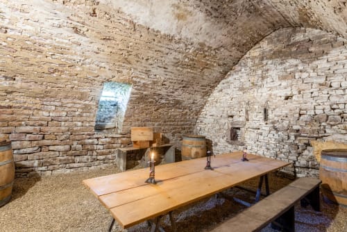 Underground stone cellar with wooden dining table, lanterns, and wine barrels at Les Maisons de Chamirey, Mercurey