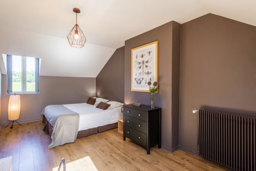 Spacious bedroom at Les Maisons de Chamirey with taupe walls, wooden floors, garden view window, and vintage-style pendant