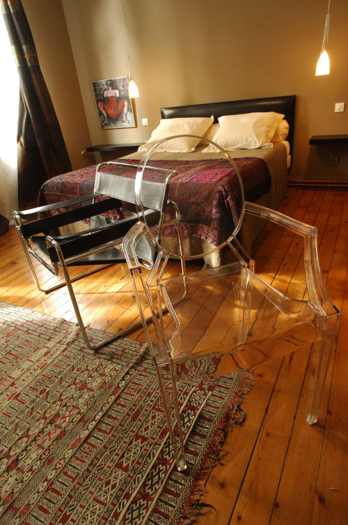 Chambre moderne du B&B Le Grand Duc à Valenciennes avec chaises transparentes, parquet et murs dorés chaleureux