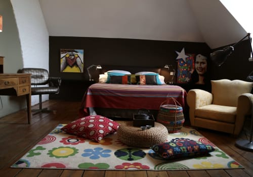Chambre mansardée colorée au Le Grand Duc B&B à Valenciennes avec tapis vibrant, literie rouge et décoration éclectique.