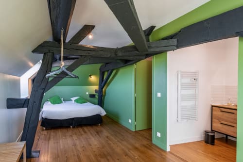 Modern bedroom with exposed beams at Les Maisons de Chamirey, featuring green walls, white bedding, wooden floors, and