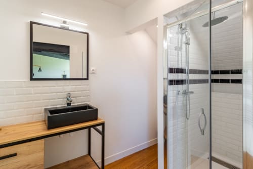 Modern bathroom at Les Maisons de Chamirey with black sink, walk-in shower with glass doors, and white subway tile walls in