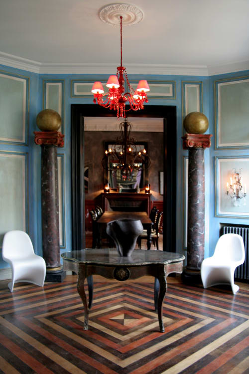 Somptueux hall d'entrée du Grand Duc aux murs bleus, lustre rouge, colonnes en marbre et sol géométrique
