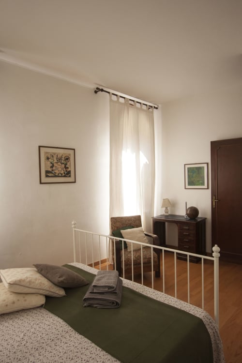 Bright bedroom in Ca Cortigiane Venice apartment with white metal bed frame, green bedding, and city view window with cream