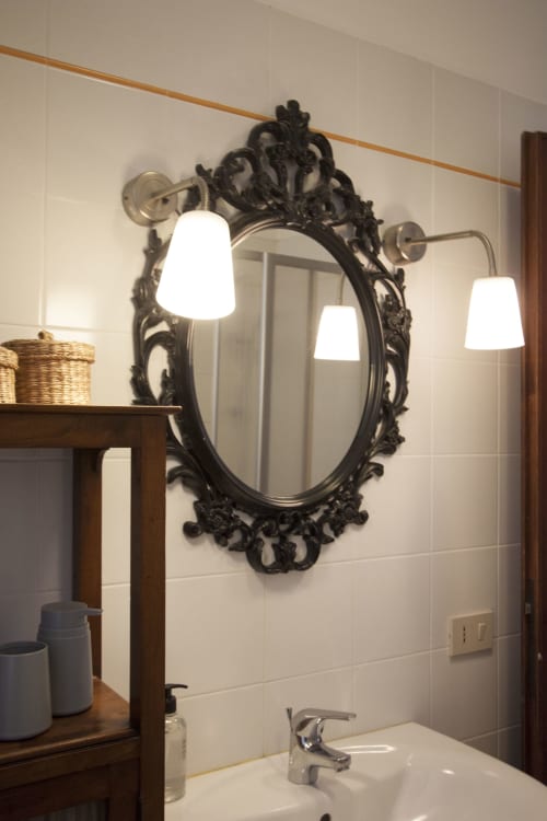Ornate black framed mirror with three wall sconces above bathroom sink at Ca Cortigiane, Venice