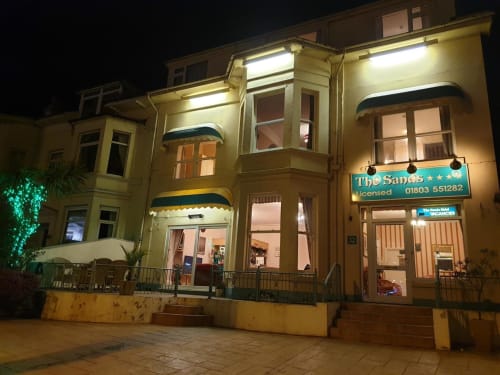 The Sands Hotel exterior at night in Paignton, illuminated cream building with blue signage and ground floor entrance