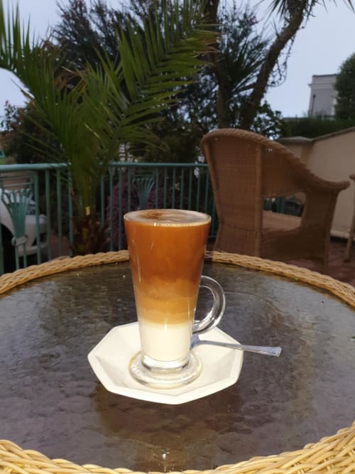 Layered coffee drink on patio table at The Sands Hotel Paignton, with palm trees and wicker furniture in background