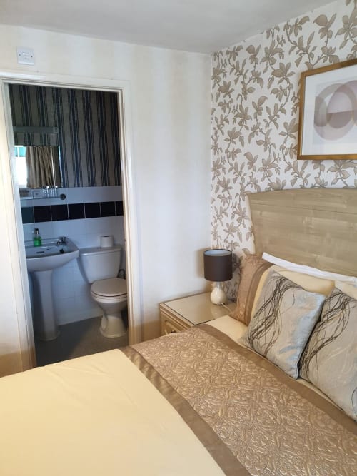 The Sands Hotel Paignton bedroom with en-suite bathroom, beige bedding, floral wallpaper, and modern furnishings