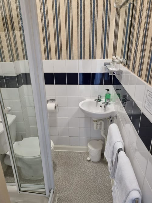 Modern bathroom at The Sands Hotel, Paignton featuring white tiles, wall-mounted sink, toilet and shower enclosure with