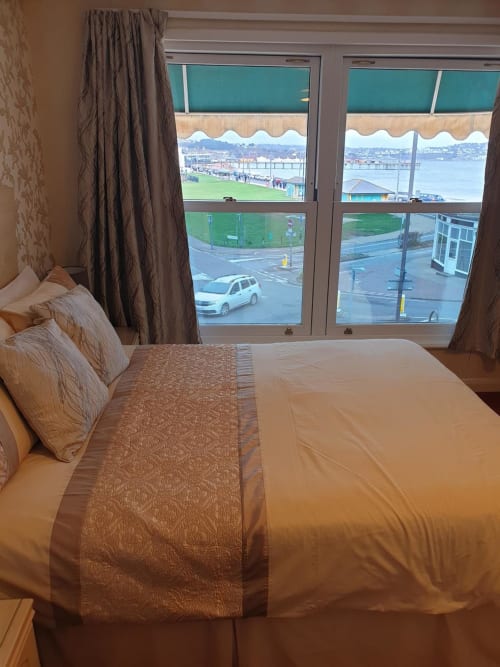 Hotel bedroom at The Sands with sea and pier views, bed with brown bedding, large windows overlooking Paignton seafront