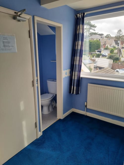 Blue and cream bathroom with toilet at The Sands Hotel, Paignton, featuring window view of residential area