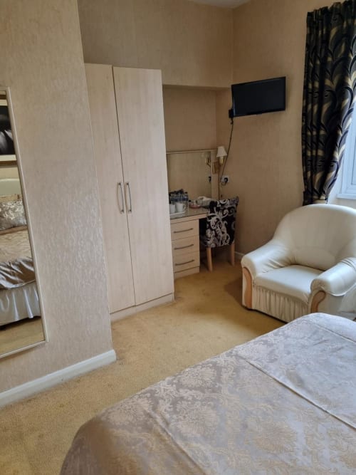 Spacious hotel bedroom at The Sands Hotel, Paignton, with double bed, wardrobe, vanity desk, armchair and wall-mounted TV