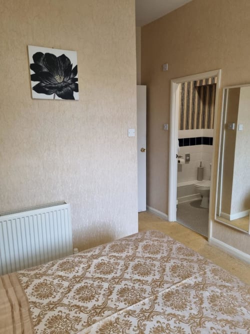 Sands Hotel Paignton bedroom with patterned bedspread, beige walls, black flower artwork, and ensuite bathroom