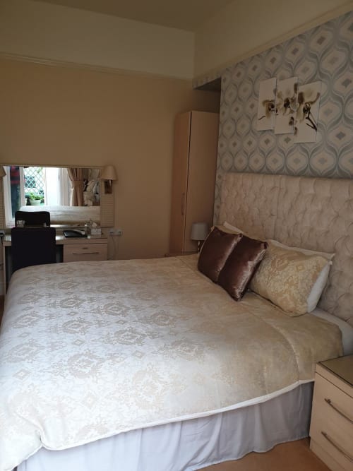 Spacious hotel bedroom at The Sands Hotel in Paignton with cream bedding, dressing table, and patterned wallpaper