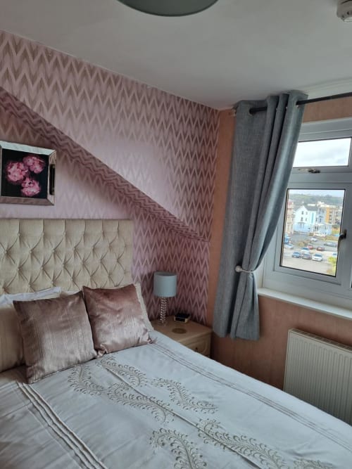 Modern hotel bedroom at The Sands Hotel, Paignton with pink patterned wallpaper, cream headboard, and sea view window